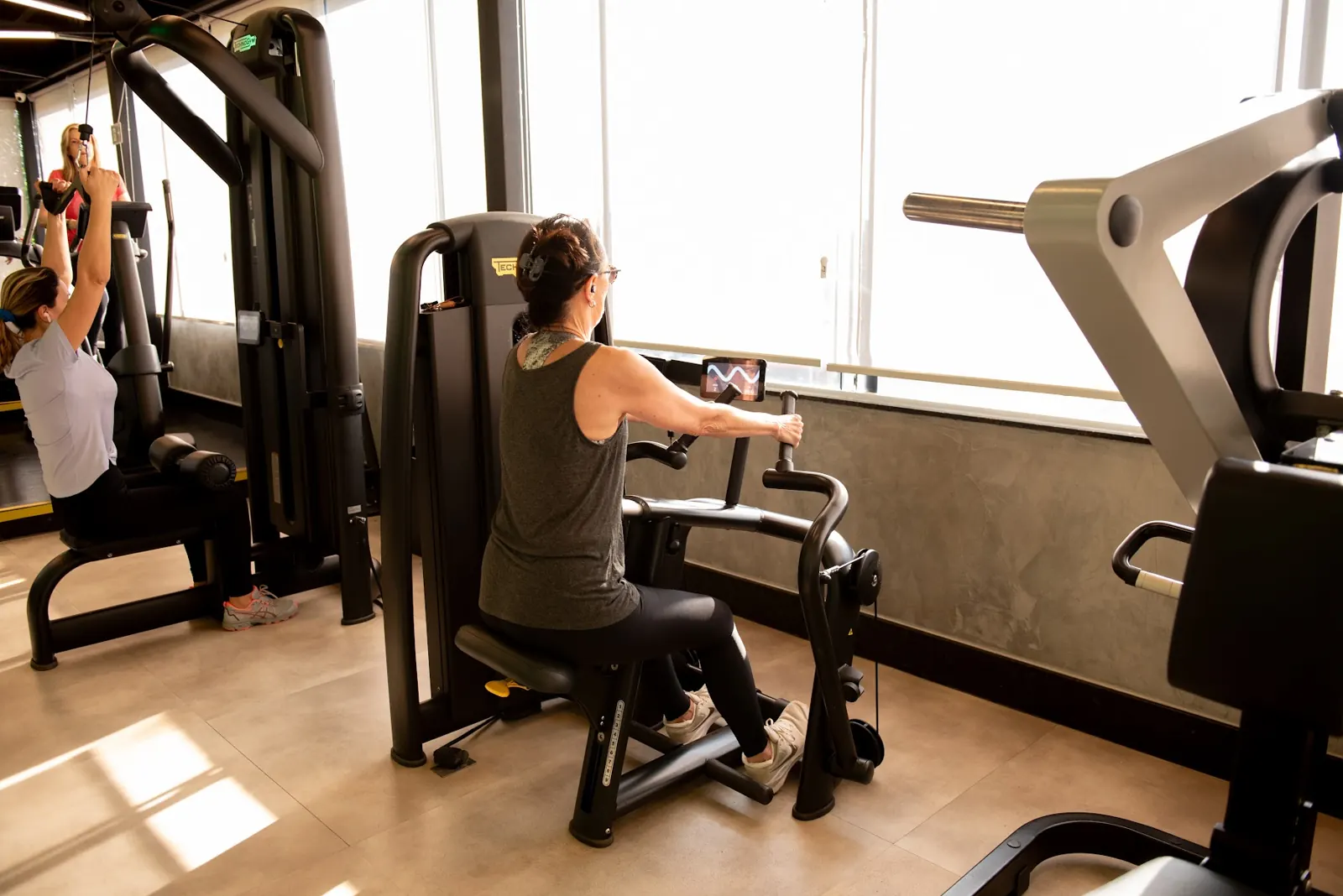 Aluna treinando em equipamento Technogym com tela digital de orientação